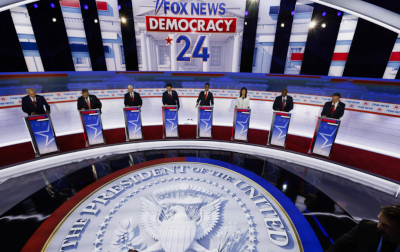 2024 republican debates. 8 podiums, each with its clown, in a semi-circle. the floor has a graphic representation of the presidential seal. it's a red white and blue soundstage. the back says fox news democracy 24 in, you guessed it, red white and blue